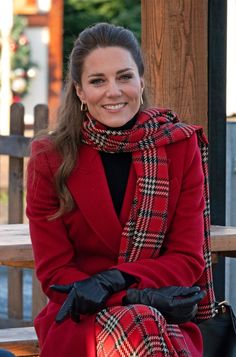 a woman in a red coat and black gloves sitting on a bench smiling at the camera