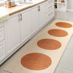 a kitchen with white cabinets and brown circles on the rug in front of the sink