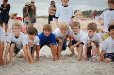 a group of young boys standing next to each other on top of a sandy beach