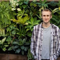 a man standing in front of a green wall with plants growing on the side and behind him