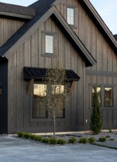 a large wooden house with black shingles on the front and side windows, along with a small tree