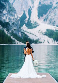 a bride and groom standing on a dock in the mountains