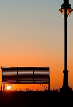 a bench sitting next to a street light at sunset