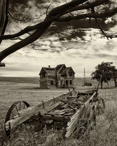 an old farm house in the middle of a field with a wooden fence around it