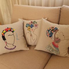 three pillows with embroidered designs on them sitting on a couch