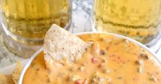 a white bowl filled with salsa and chips next to two glasses of beer on a table