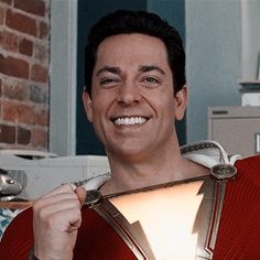 a man in a superman costume holding up a light bulb to his chest and smiling at the camera