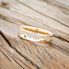 a gold wedding band with green stones sits on an old wooden table, ready to be used as a ring