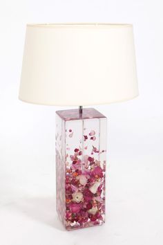 a lamp that is on top of a table with pink flowers in it and a white shade