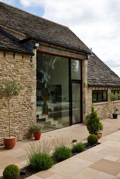 a stone building with potted plants on the outside and large glass windows in front