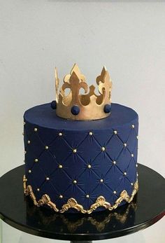 a blue and gold cake with a crown on top is sitting on a glass table