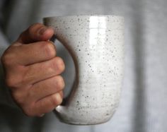 a person holding a white coffee cup in their left hand with speckles on it