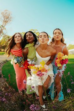 four women in dresses are sitting on the grass and one woman is holding a bouquet