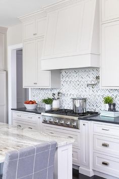 a kitchen with white cabinets and marble counter tops