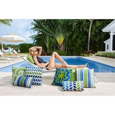 a woman sitting in a chair next to a swimming pool with pillows on the floor