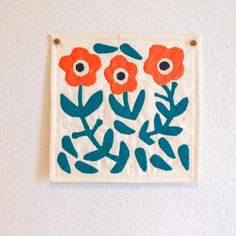 an orange and blue flower on a white wall hanging from a hook in a room