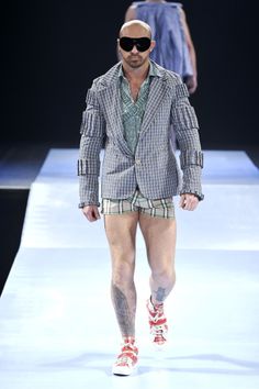 a man walking down a runway in shorts and a jacket with sunglasses on his head