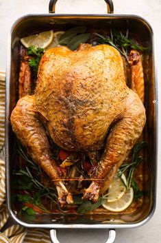 a roasted turkey in a roasting pan with herbs and lemons