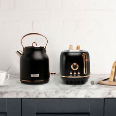 two black tea kettles sitting on top of a counter next to a cup and saucer