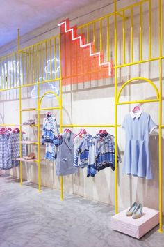 clothes are displayed on yellow racks in a clothing store with blue and white shirts hanging from them