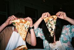 two people holding up slices of pizza in front of their faces, both with different toppings