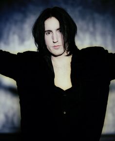 a man with long hair and black shirt holding his arms out in front of him