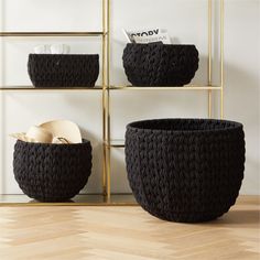 three black woven baskets sitting on top of a wooden floor next to a book shelf