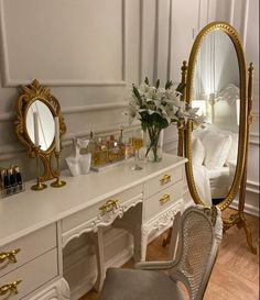 a white desk topped with a mirror next to a chair and a vase filled with flowers