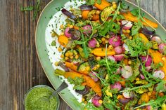 a green plate filled with vegetables next to a small bowl of pesto on the side