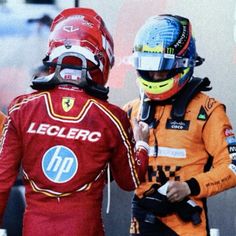 two men in racing gear standing next to each other with helmets on their heads and one wearing a helmet