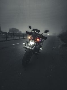 the motorcycle is parked on the side of the road in the foggy night time