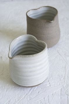 two white vases sitting next to each other on top of a tablecloth covered floor