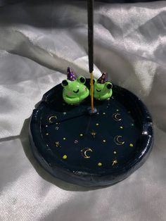 two green frogs sitting on top of a black clock with stars and moon decorations around it