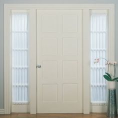 a vase with flowers in it sitting next to two white doors that have glass panels on them