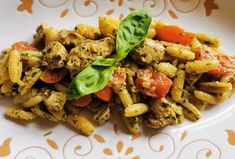 a white plate topped with pasta covered in meat and vegtables next to a leafy green garnish