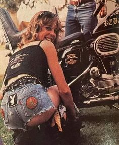 a woman sitting on the ground next to a motorcycle and another man standing behind her