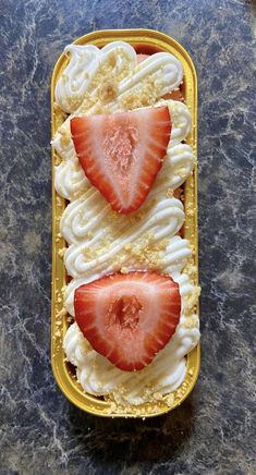 two strawberries are in a yellow container on a table with white icing and whipped cream