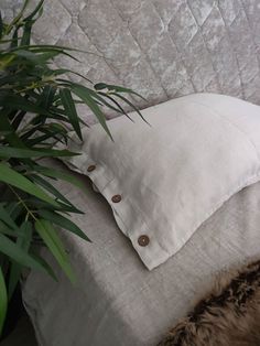 a white pillow sitting on top of a bed next to a plant