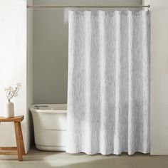 a white shower curtain in a bathroom next to a bathtub and wooden stools