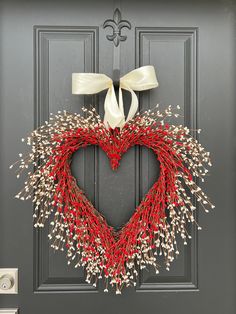 a heart shaped wreath with white bow hanging on a door