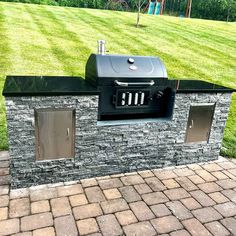 an outdoor bbq grill in the middle of a brick patio with grass behind it