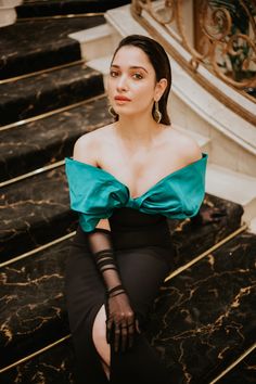 a woman sitting on the steps wearing black gloves and a green top with ruffled sleeves