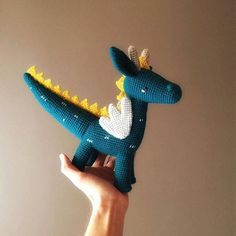 a hand holding a small stuffed toy in the shape of a dinosaur with a crown on it's head