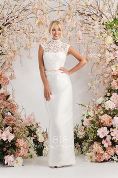 a woman standing in front of flowers wearing a white dress with an open neckline