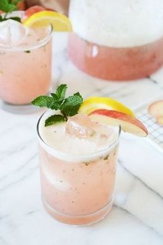 two glasses filled with drinks sitting on top of a table next to an apple slice