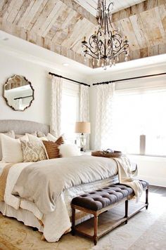 a bedroom with a bed, ottoman and chandelier