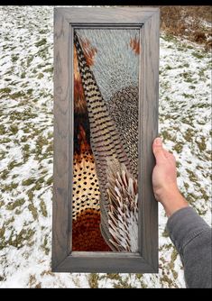 a person holding up a framed artwork in the snow with their hand on it's side