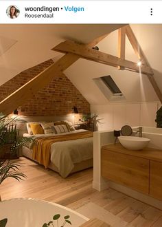 a bed room with a neatly made bed next to a bathtub and sink under a slanted roof