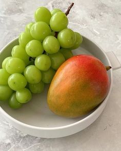 a white bowl filled with green grapes and a ripe mango sitting on top of it