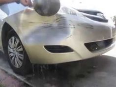 a person washing a silver sports car on the side of the road with water coming out of it